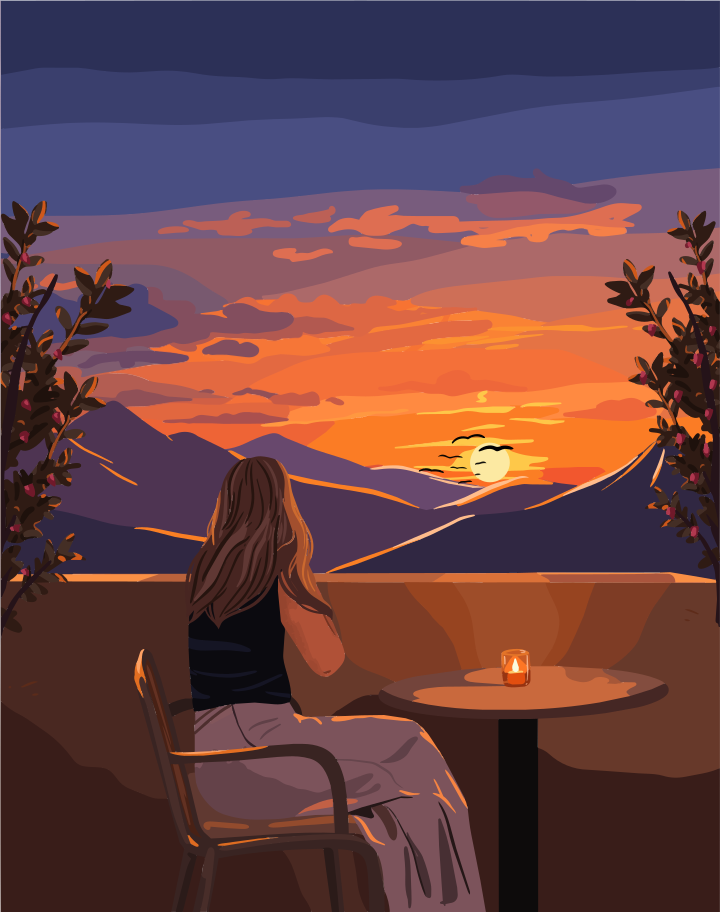 A person sitting at a table on a balcony overlooking mountains at golden hour